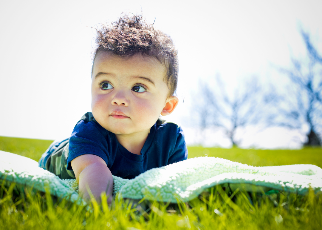A baby in blue on a green blanket in the grass.