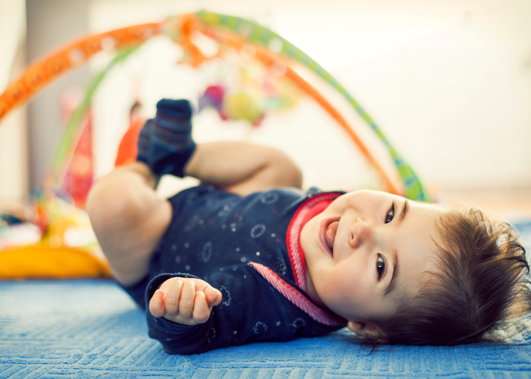 A smiling baby under a play gym.