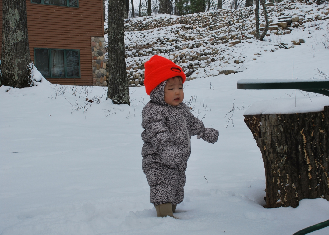 A baby in a leopard puffer suit and neon hat in the snow.