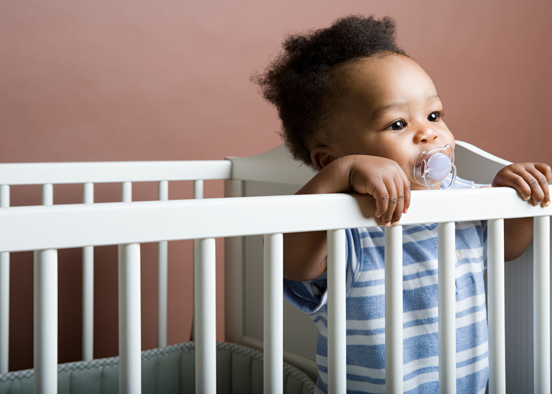 A baby in a blue and white striped outfit standing in a crib.