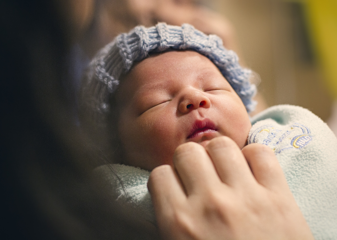 A baby boy wrapped in a swaddle wearing a blue hat.