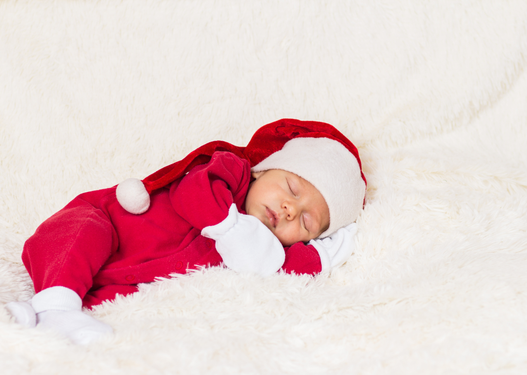 A baby boy sleeping in a red santa suit and hat.