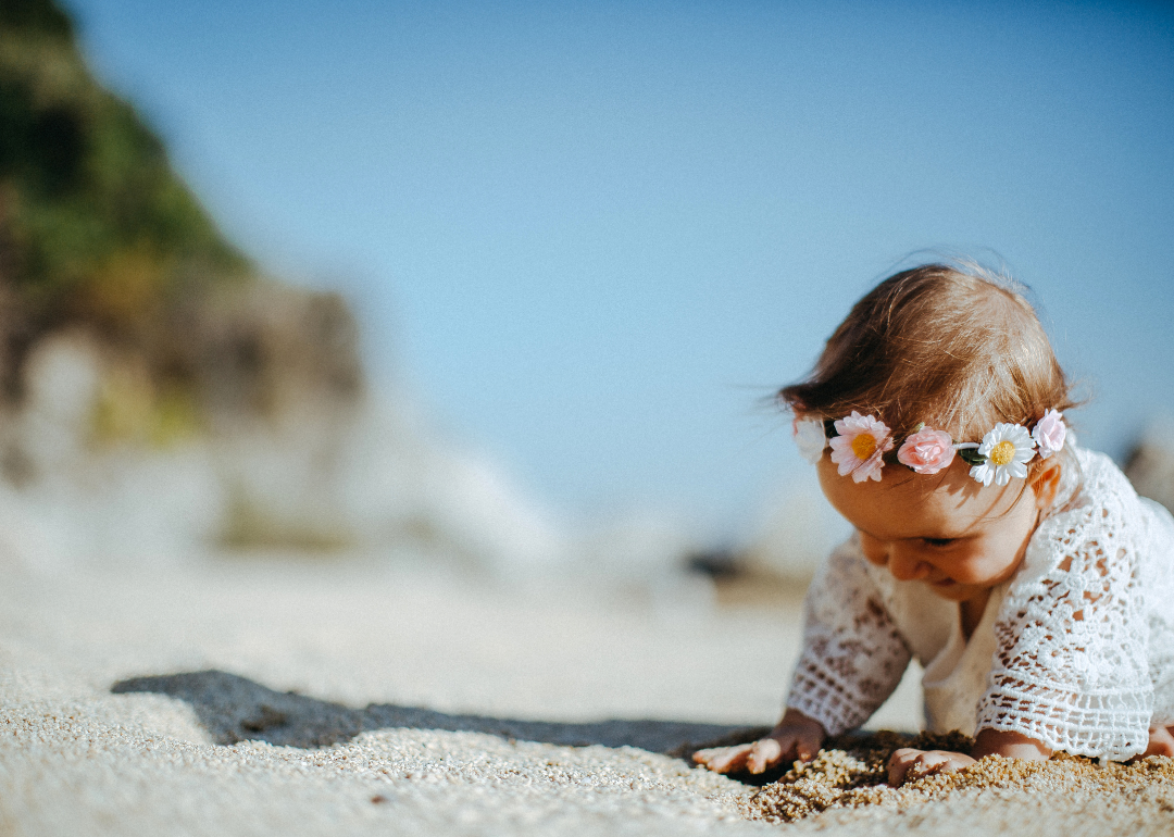 A baby girl on the beach wearing a crochet outfit and a flower crown.