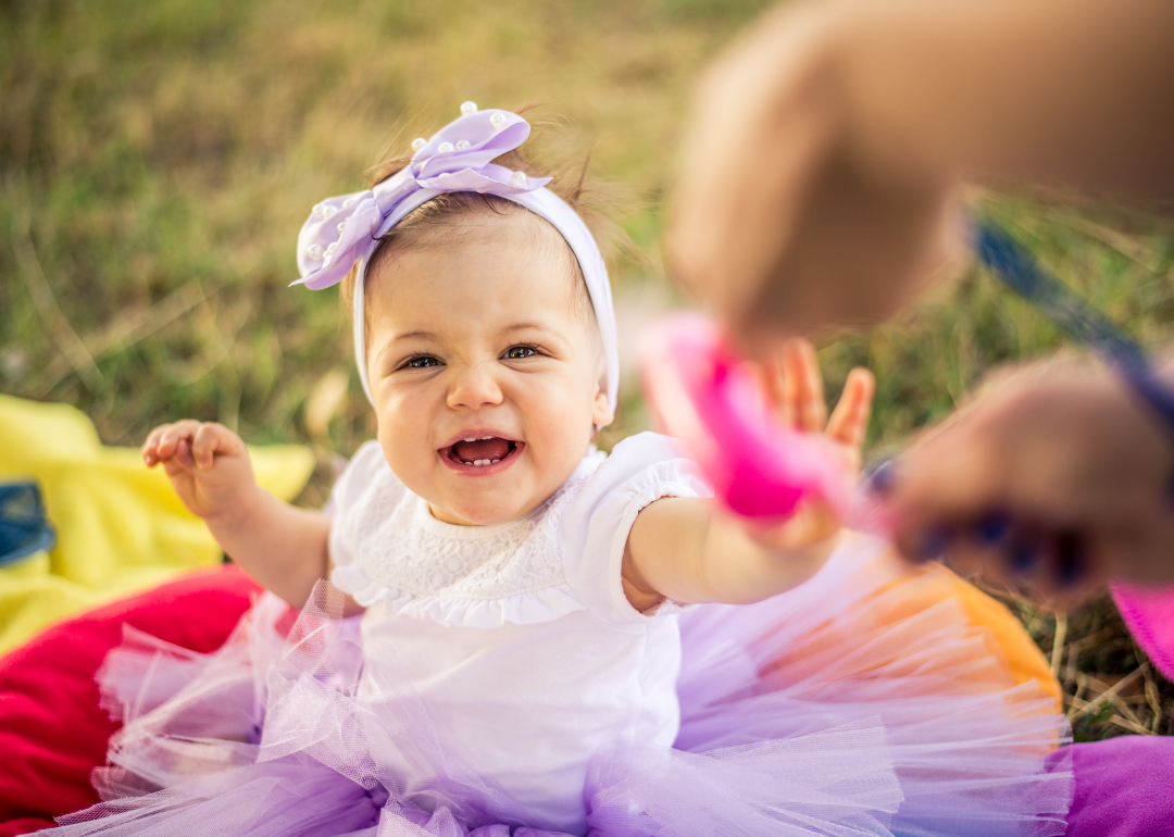 A smiling baby outside in a purple tutu.