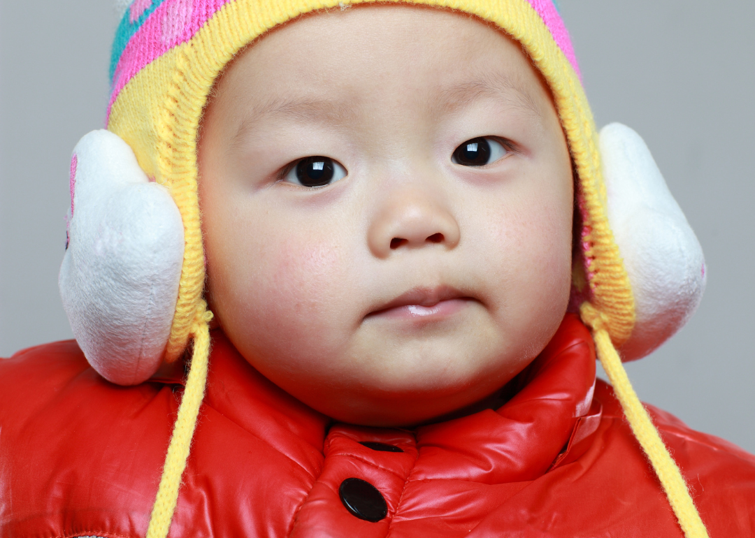 A baby boy in a red snow jacket and colorful hat.