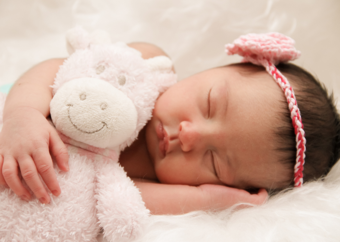 A sleeping baby girl with a pink bow and plush animal.