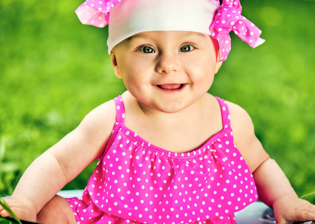A baby girl outside in a pink polka dot outfit.