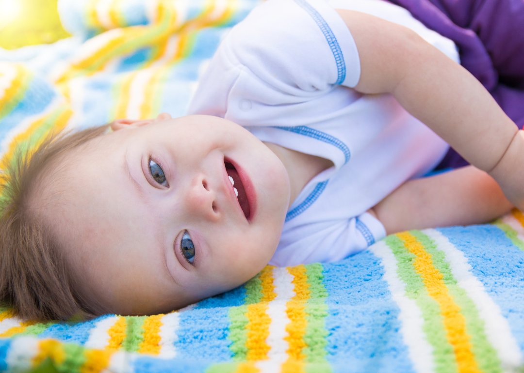 A baby boy lying on a striped blanket outside.