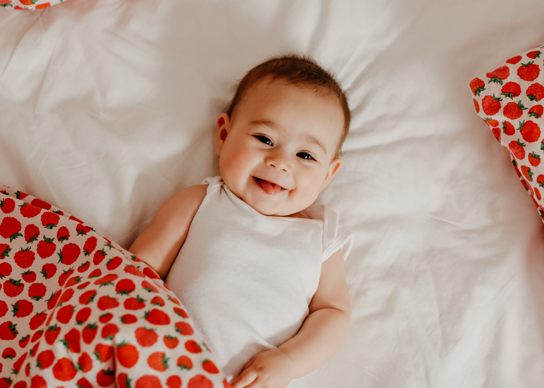 A smiling baby girl holding a strawberry blanket.