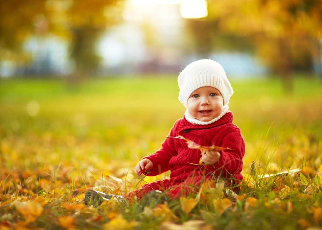 A baby boy in a red knit suit in the Fall leaves.