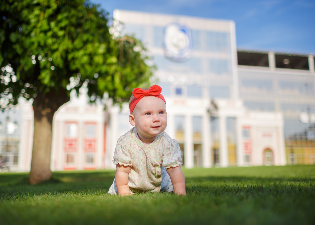 A baby girl on the grass outside in an orange headband.