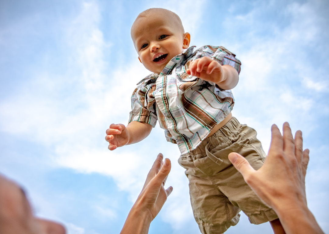 A baby boy in a plaid shirt being thrown up in the air.