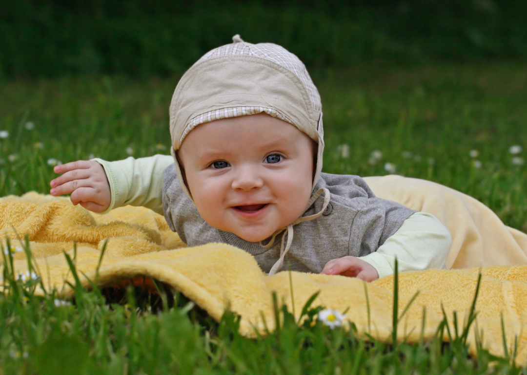 A baby boy lying on a yellow blanket in the grass.