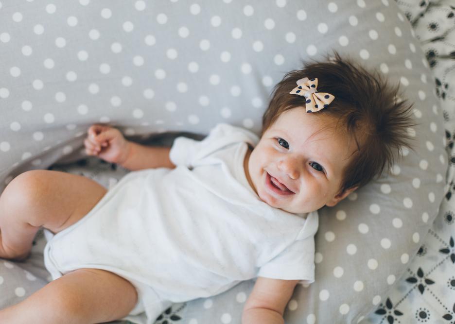 A baby girl with a pink bow smiling in her crib.