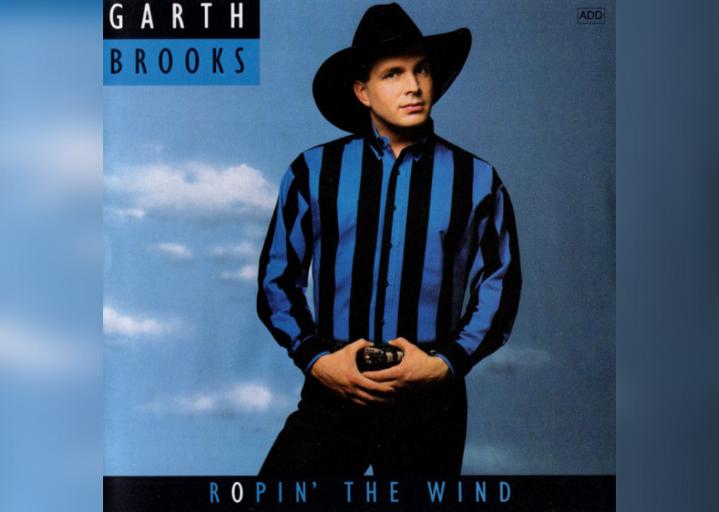 Garth Brooks posing in front of a blue sky wearing a black cowboy hat and blue and black striped western shirt.