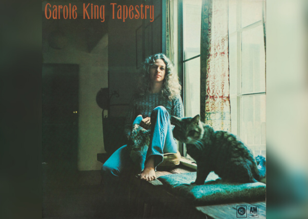 Carole King sitting in a window seat with a cat.
