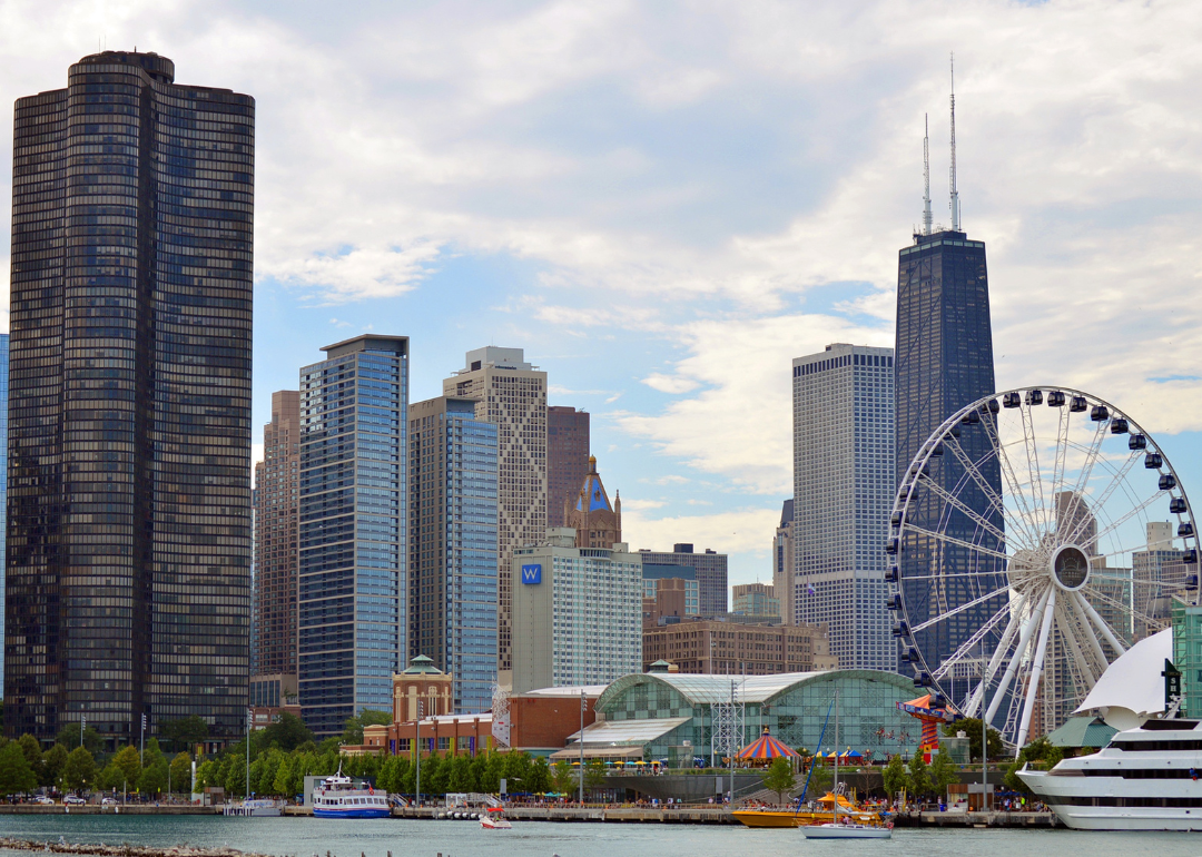 A ferris wheel on the water with skyscrapers in the background.