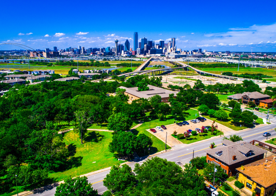 An aerial view of green trees and bridges with the Dallas skyline in the background.