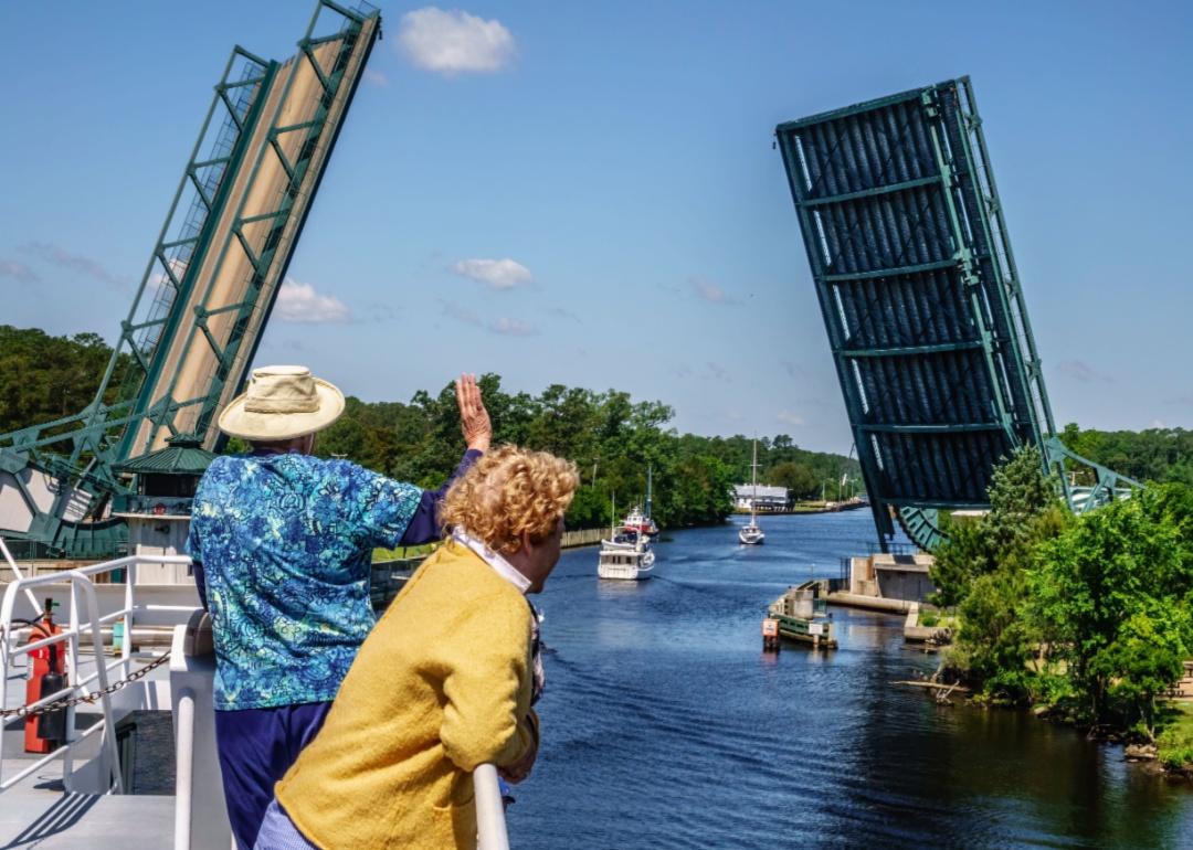 Two people waving at boats as a drawbridge opens.