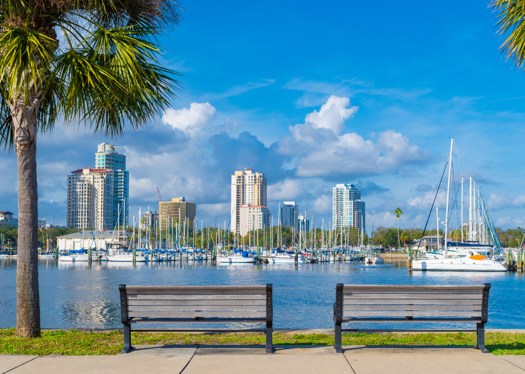 Two park benches with a view of boats on the water and buildings.