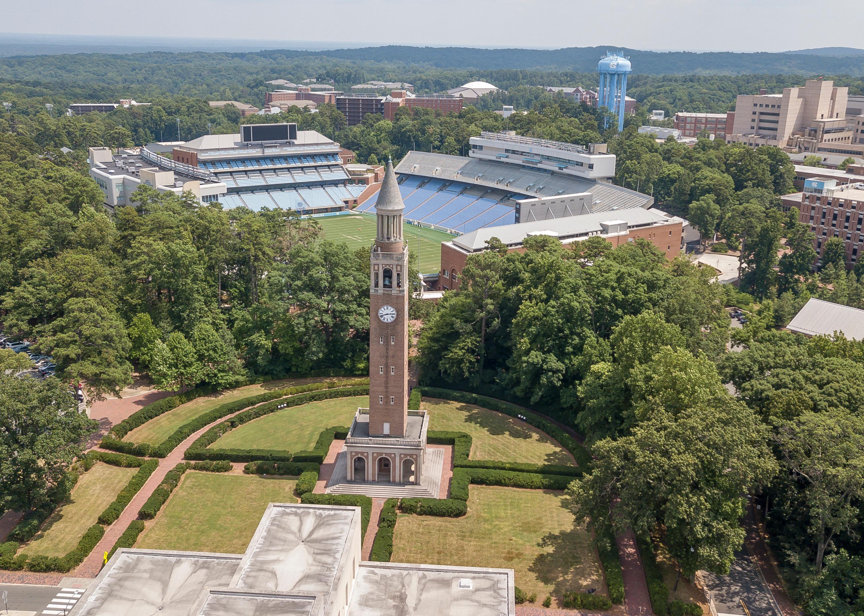 An aerial view of a clocktower and a stadium surrounded by trees.
