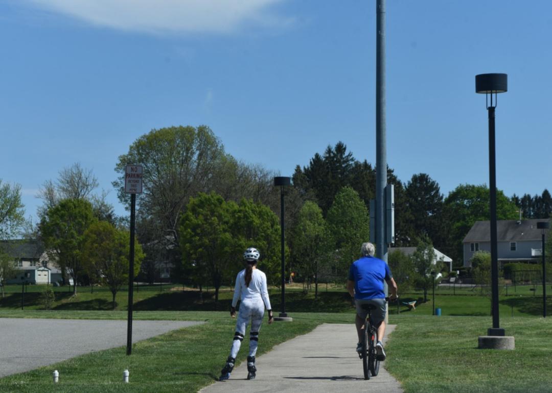 A woman rollerblades next to a man bicycling near homes.