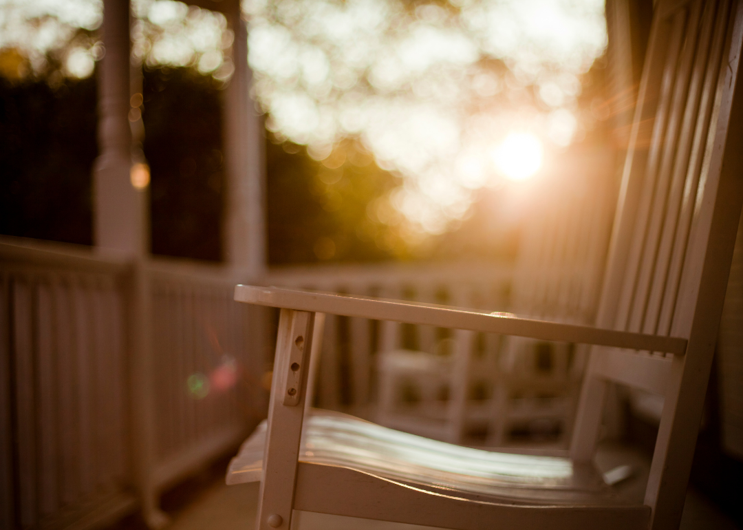 A rocking chair on a front porch with the sun in the background.