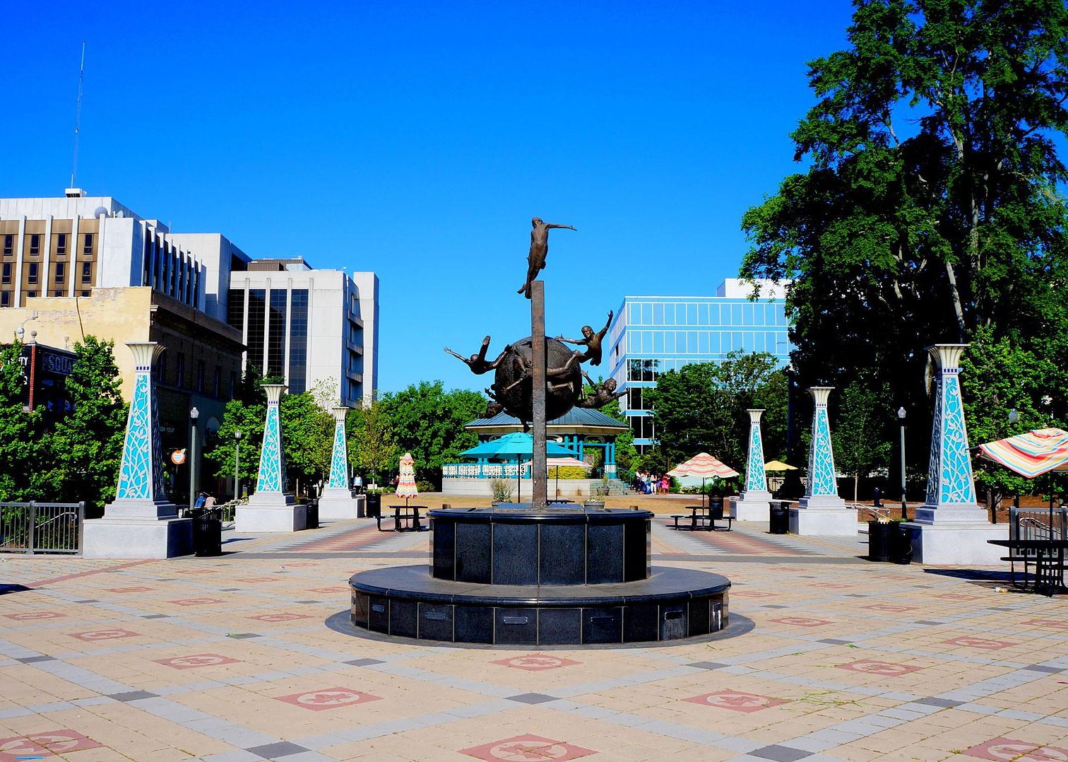An art statue of people flying centered in a town square surrounded by blue pillars.