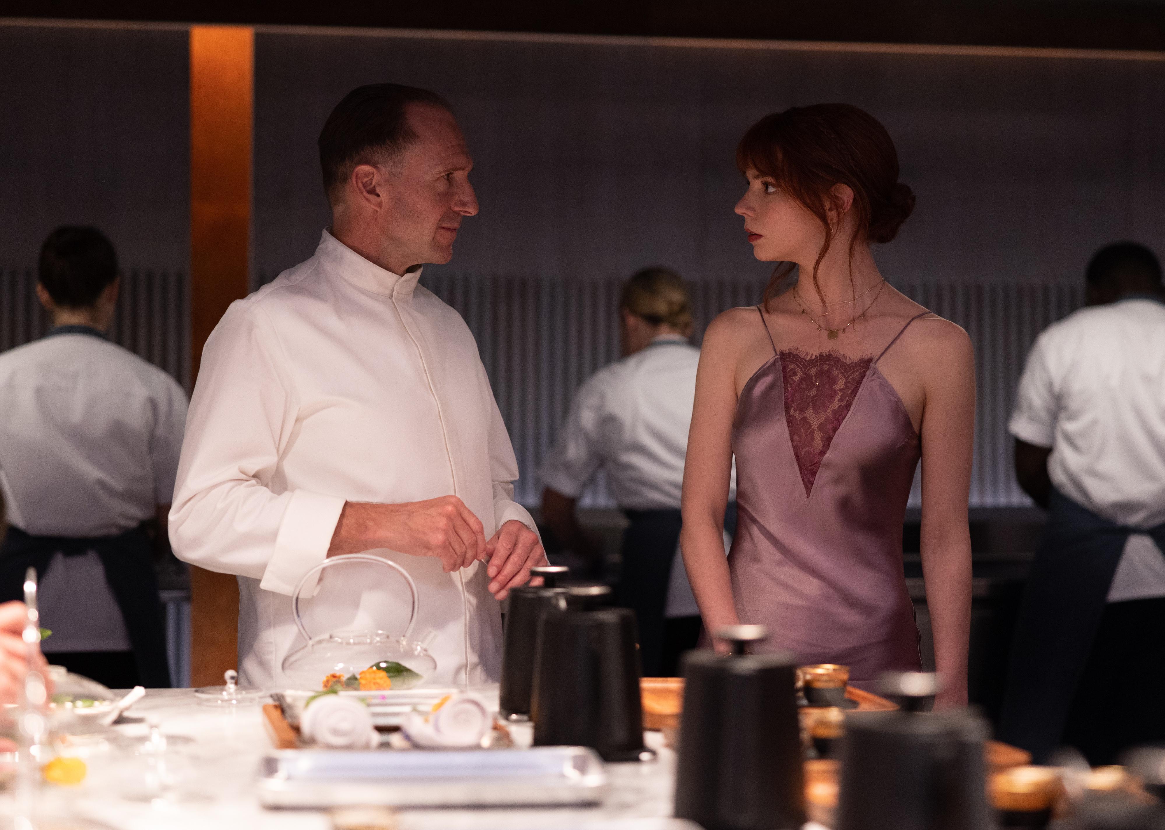 Ralph Fiennes as a chef talking to Anya Taylor-Joy in a silk gown at a party