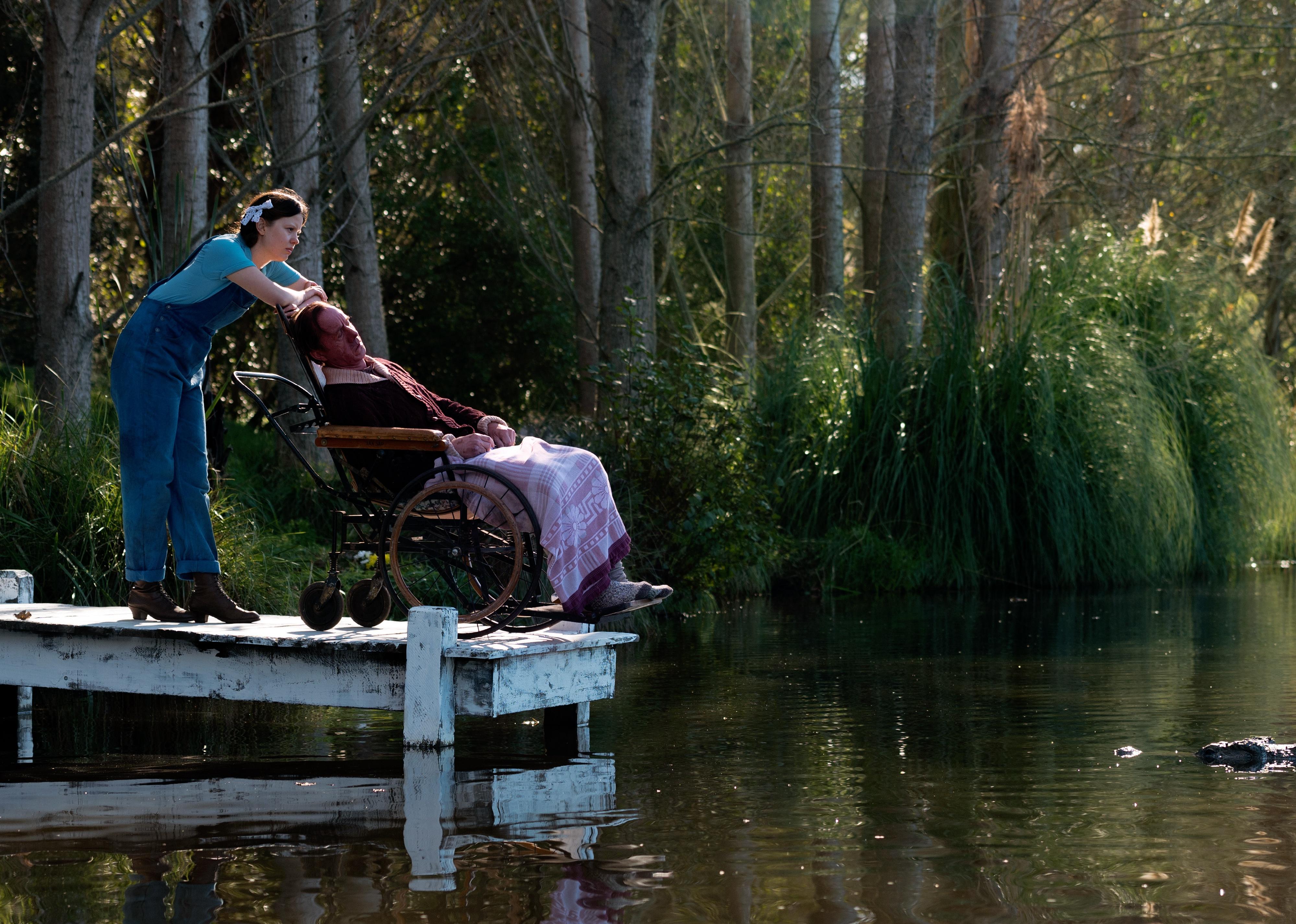 A young woman in overalls standing on a dock with a man in a wheelchair