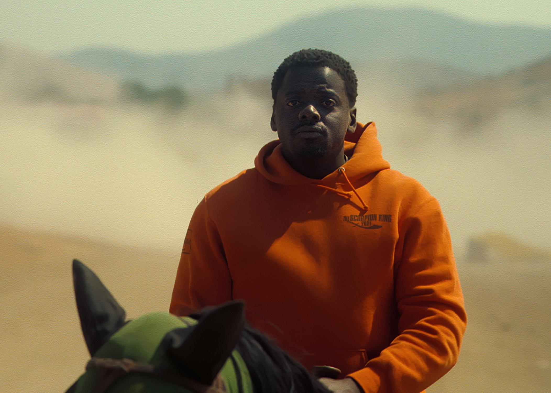 Daniel Kaluuya riding a horse in an orange hoodie