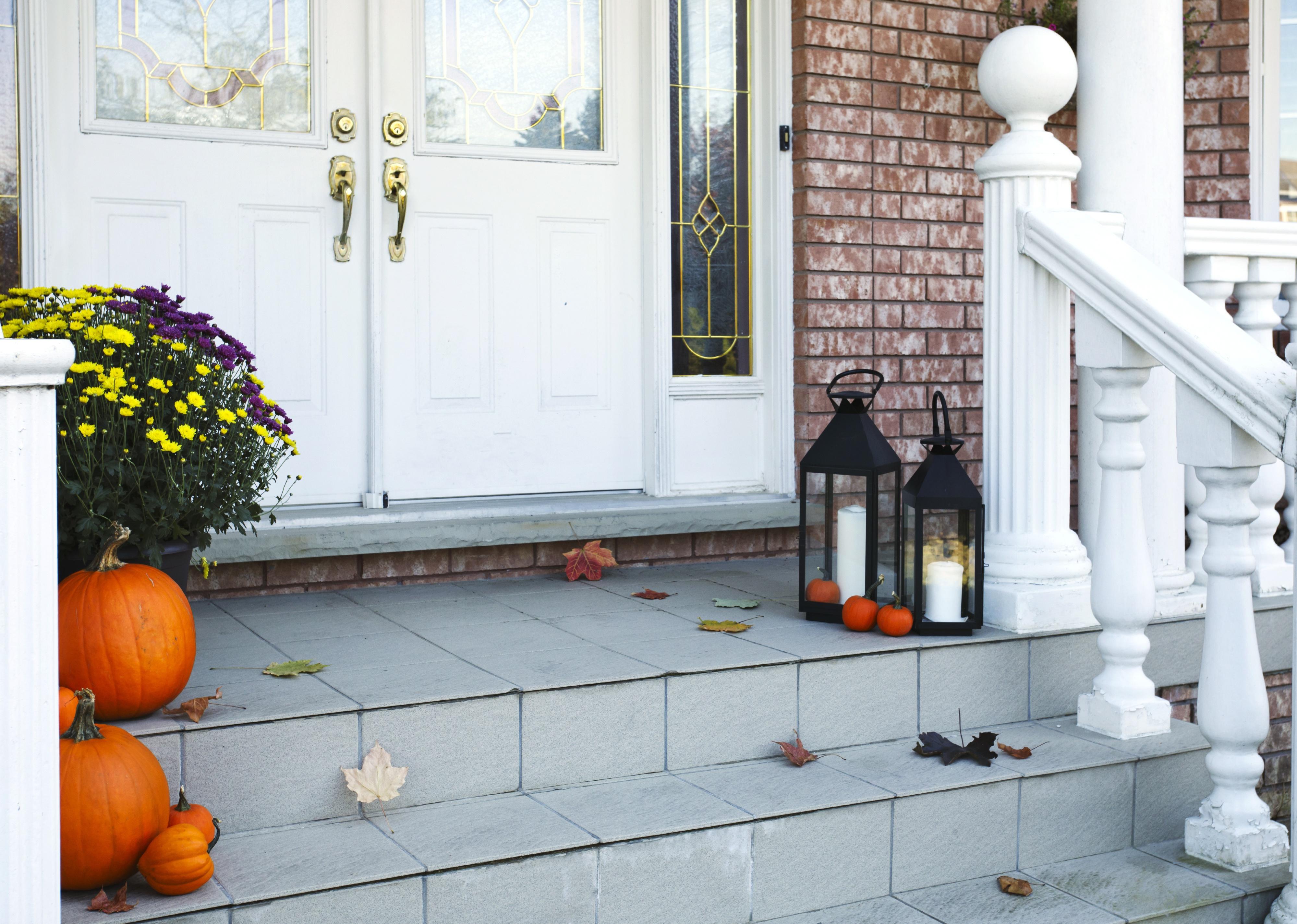 A porch with a white front door and railing and pumpkins on the stairs.