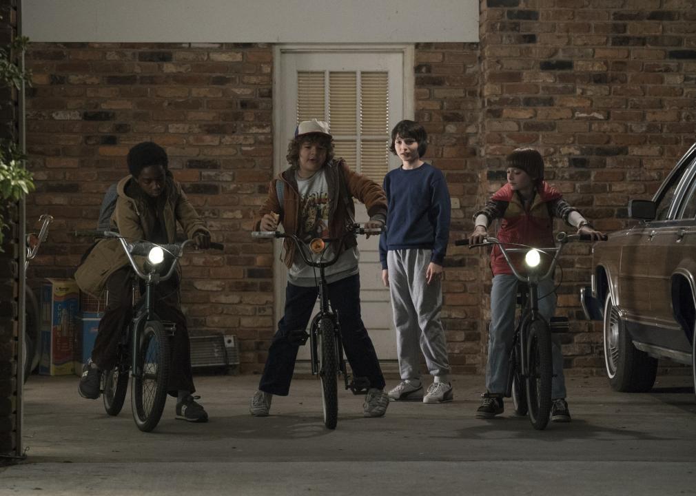 Caleb McLaughlin, Finn Wolfhard, Noah Schnapp, and Gaten Matarazzo with bikes next to a station wagon.