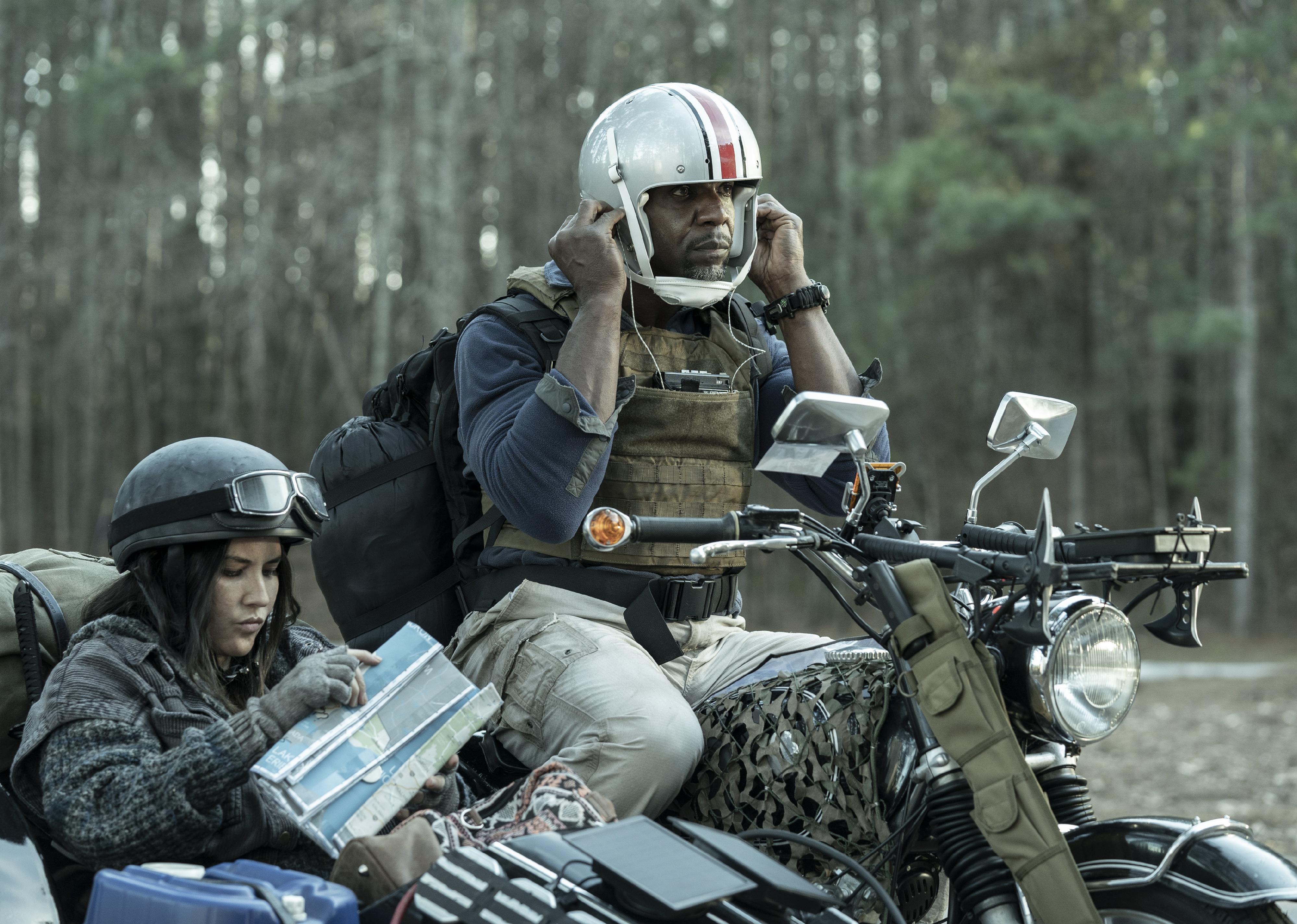 Terry Crews and Olivia Munn wearing makeshift survival gear riding a motorcycle with sidecar.