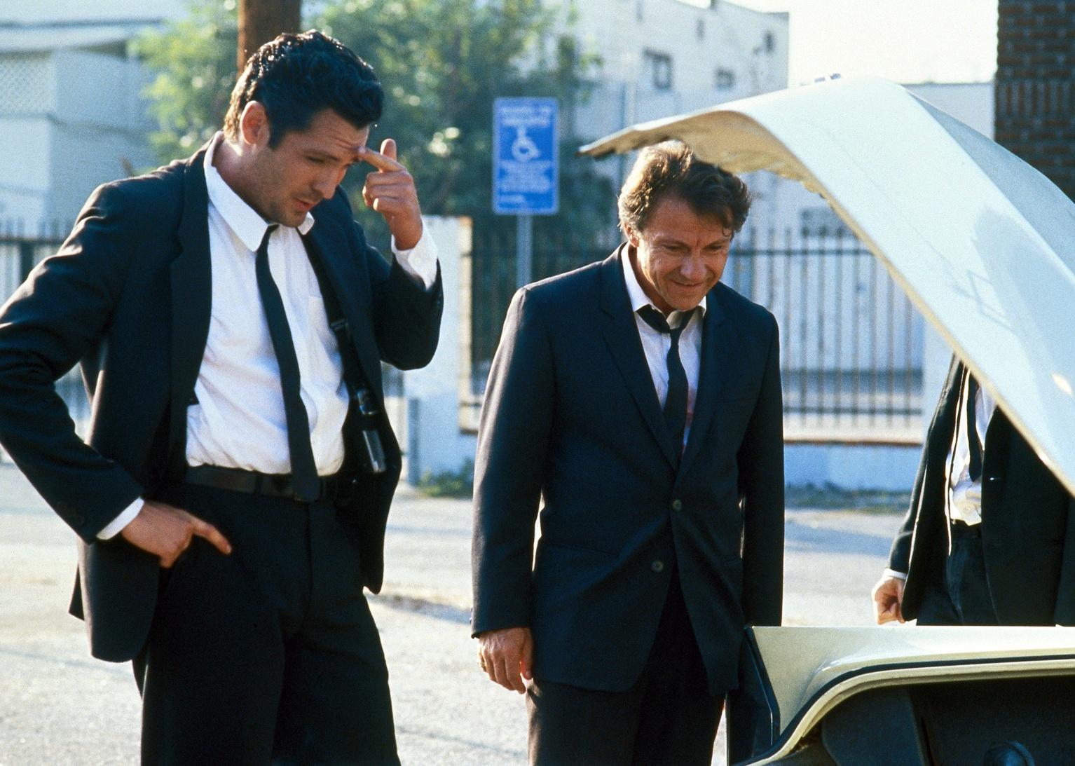 Harvey Keitel and Michael Madsen wearing black suits and looking into the trunk of a car.