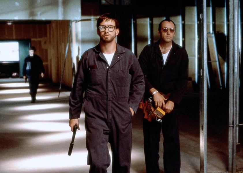 Kevin Spacey and Stephen Baldwin walking down a hallway in jumpsuits with guns.