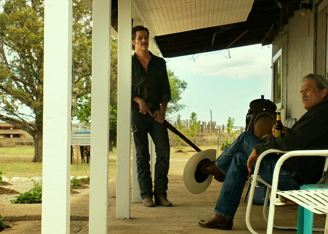 Jeff Bridges and Chris Pine, holding a gun,  on the front porch of a house in the country.