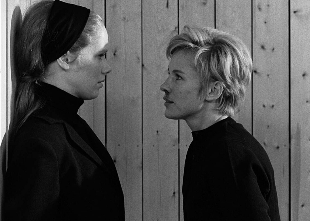 A woman in black with a bloody nose standing close to the face of another woman up against a wall.