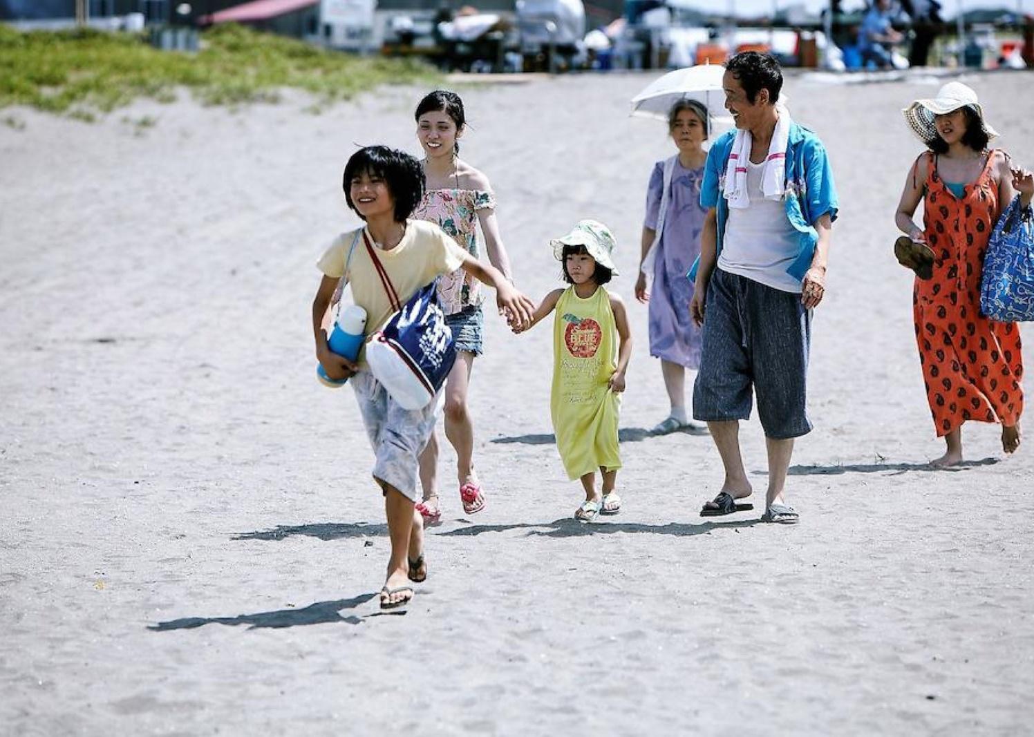A family of kids and adults walks on the beach.