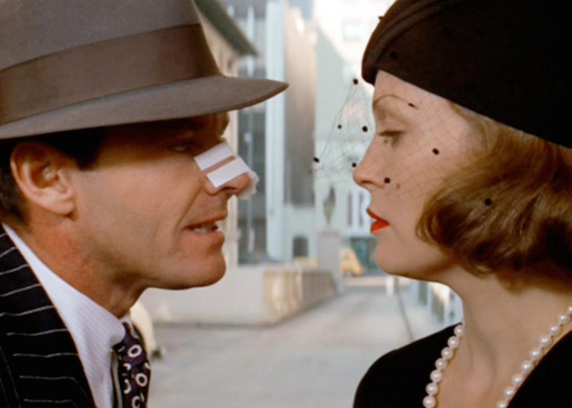 Jack Nicholson, with tape on his nose, and Faye Dunaway, wearing a black mourning veil and hat, stare at each other.