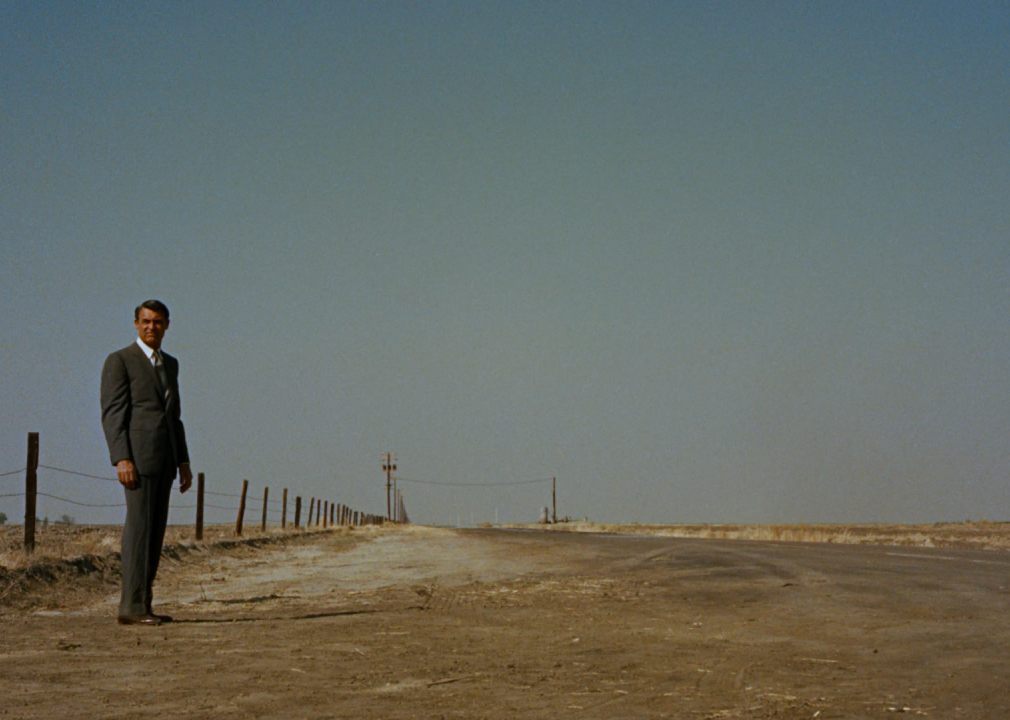 A man standing on a desolate road lined by a fence.