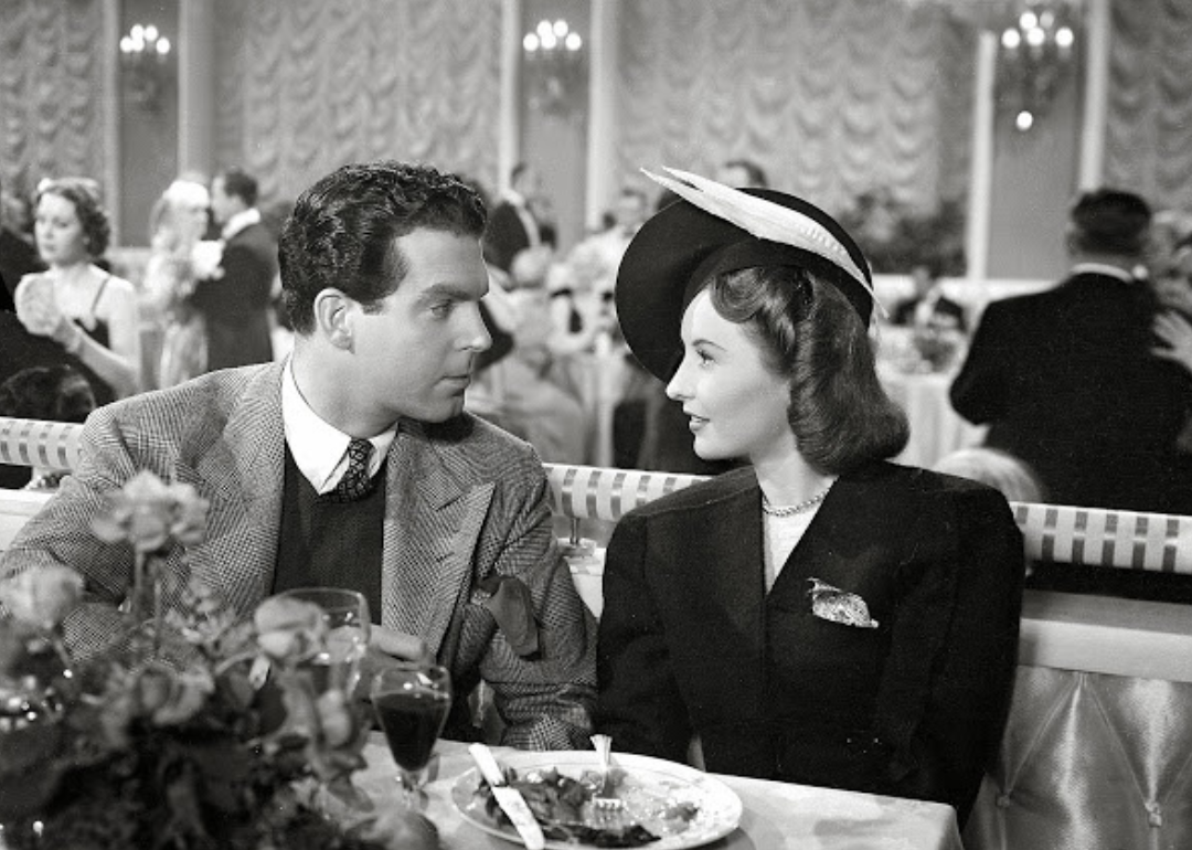 A man and woman dressed up in a restaurant looking longingly at one another.