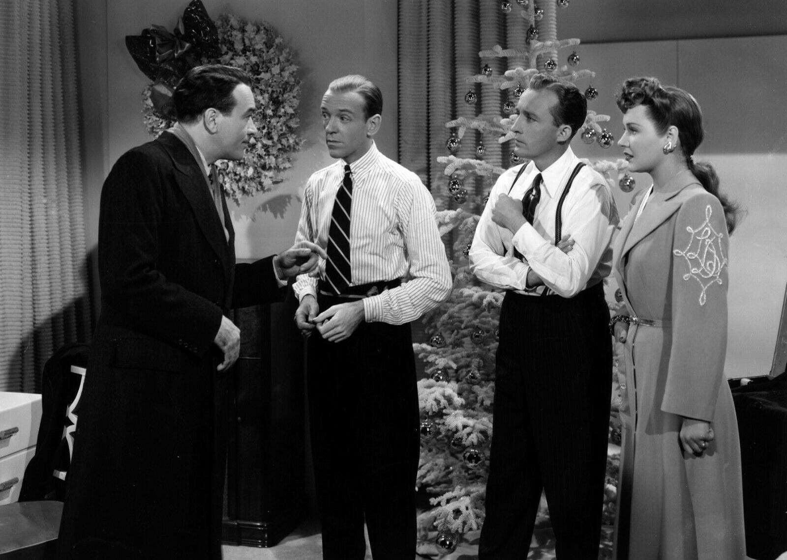 Fred Astaire and Bing Crosby talking with a man and woman in front of Christmas trees.