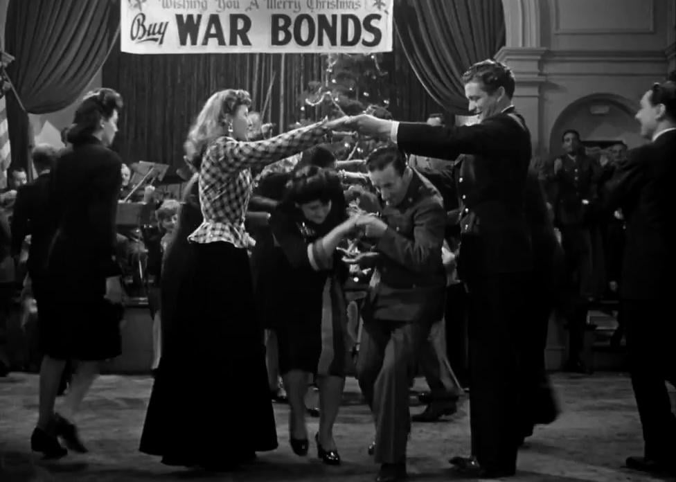 Barbara Stanwyck and Dennis Morgan holding their hands together in the air while other dancers go under them.
