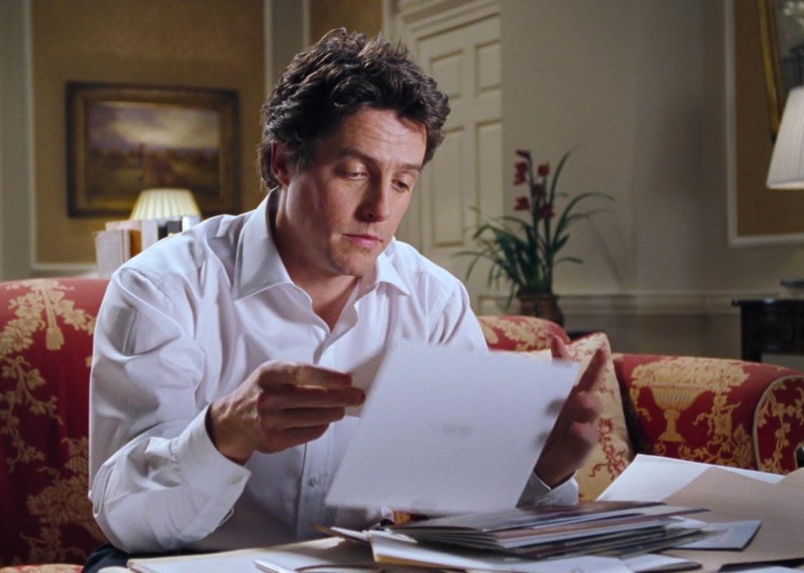 Hugh Grant reading on a couch in front of a Christmas tree.