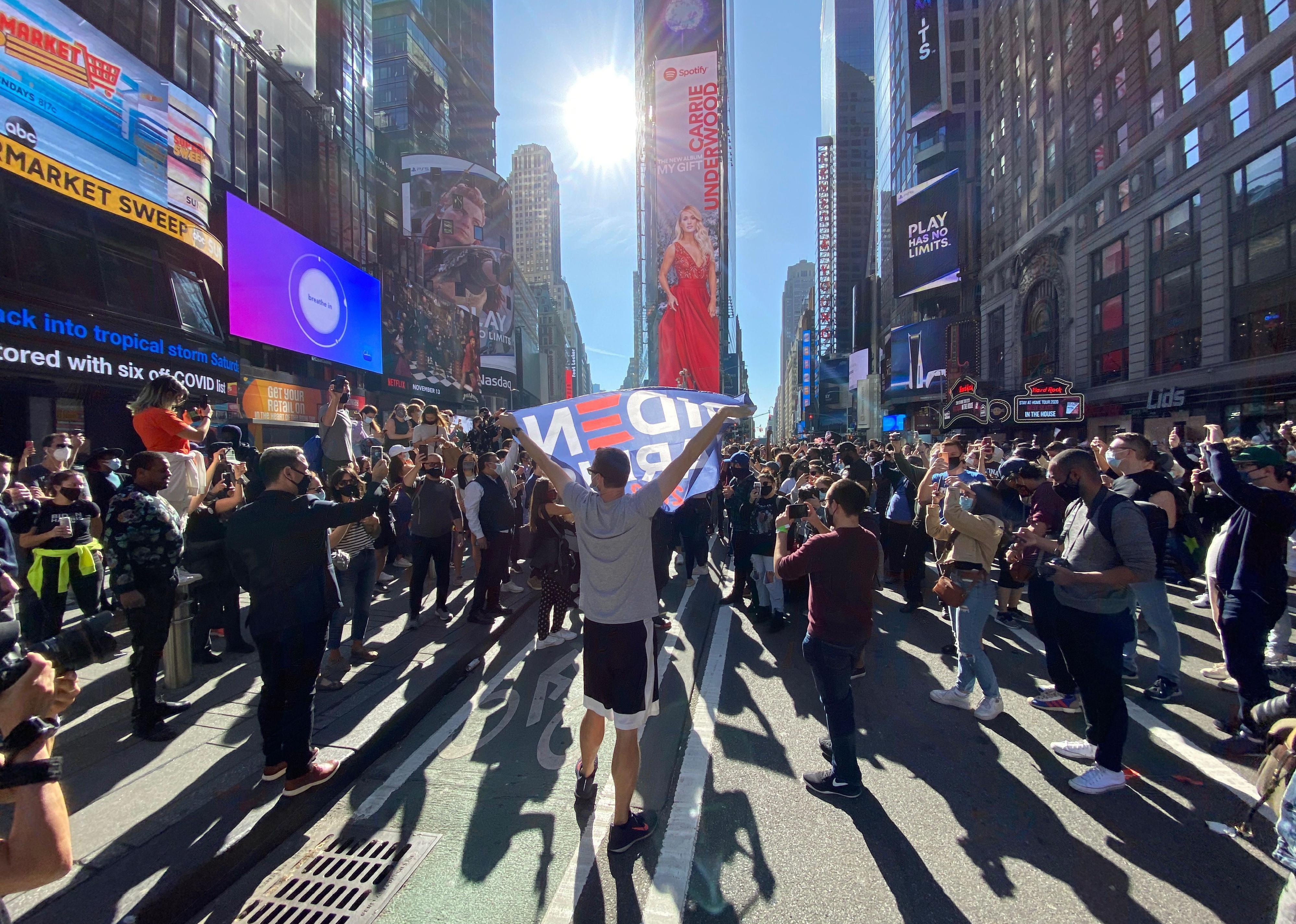 People celebrate at Times Square in New York with a Biden flag.