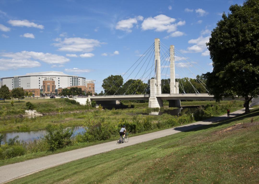 A cyclist riding along a river near a bridge.