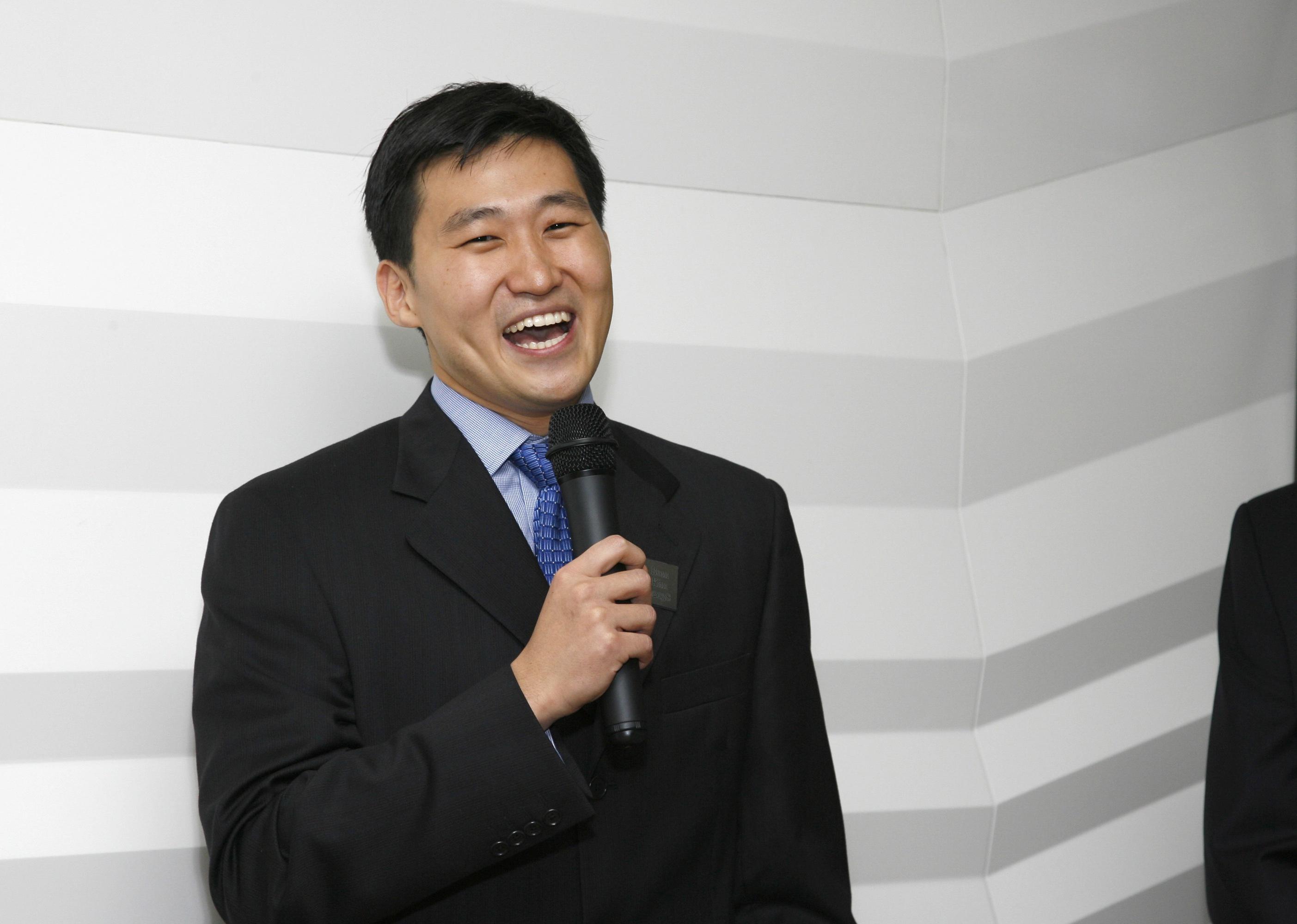Bom Kim smiling in a suit with a microphone in hand.
