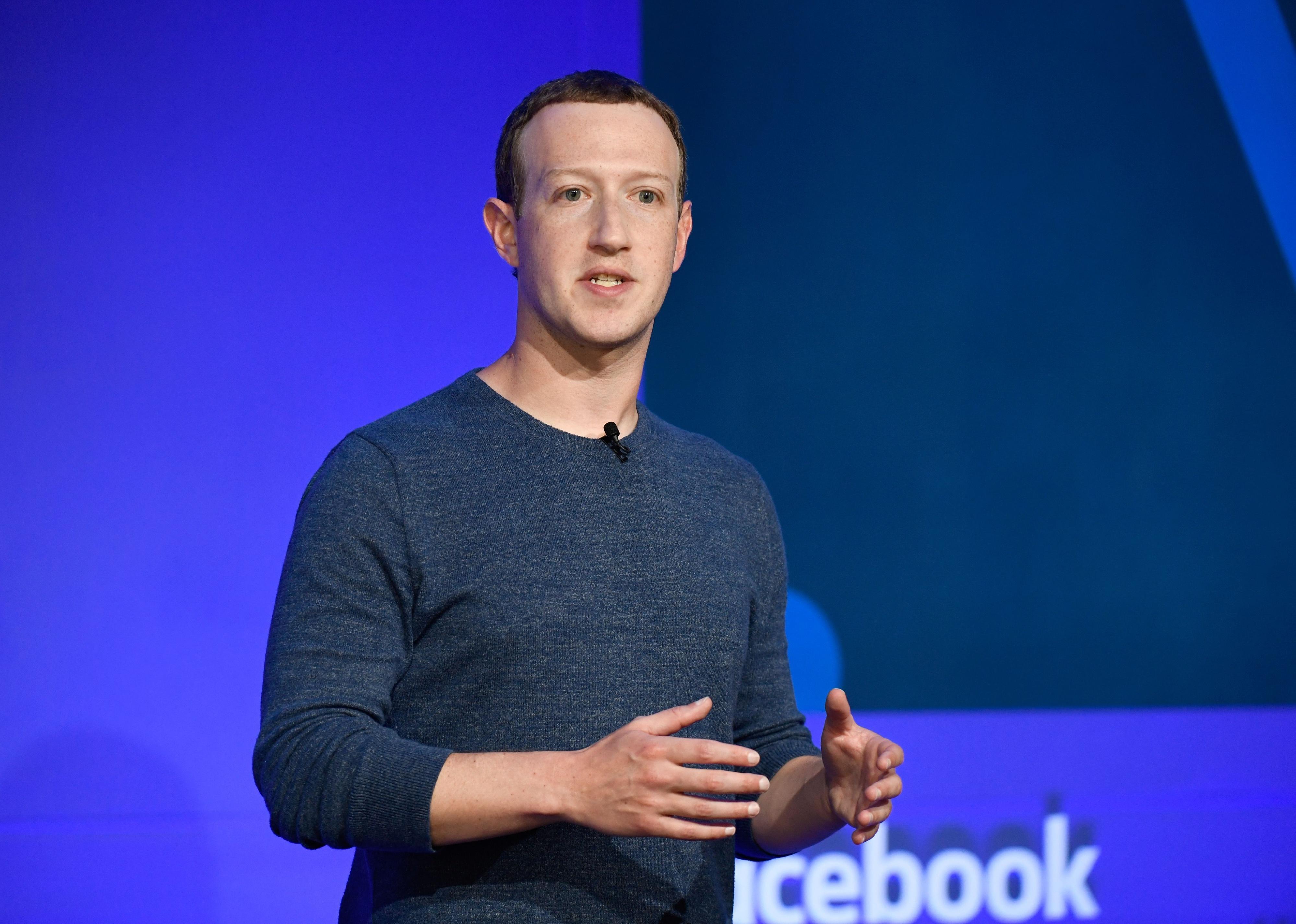 Mark Zuckerberg speaking in front of a blue Facebook background.
