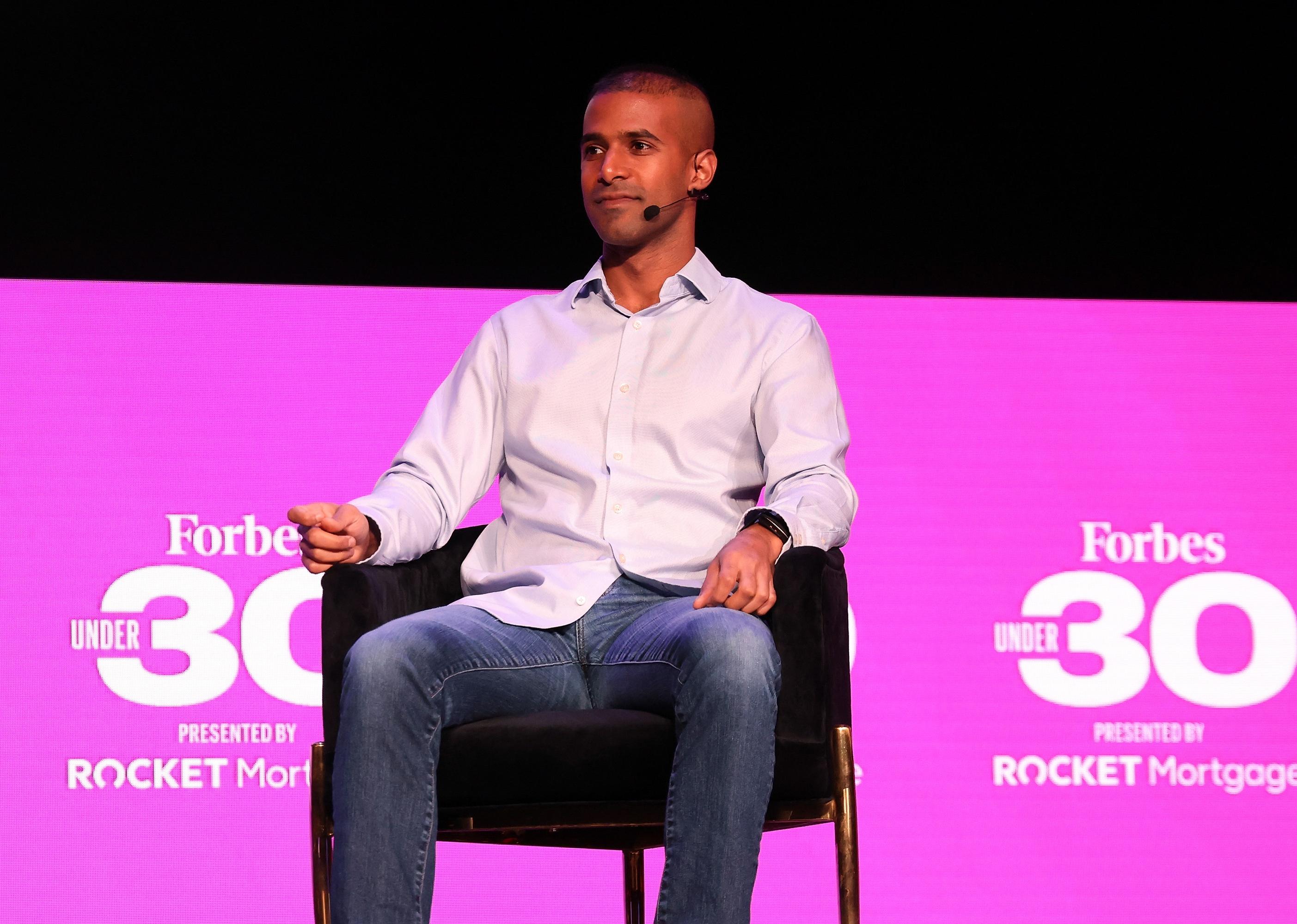 Nikil Viswanathan in front of a pink background onstage.